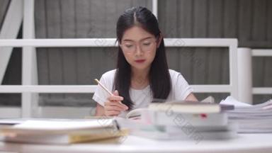 亚洲学生妇女读图书馆的书籍在大学。年轻的本科生女孩做家庭作业，读课本，努力学习知识和教育在课桌在大学校园的概念.